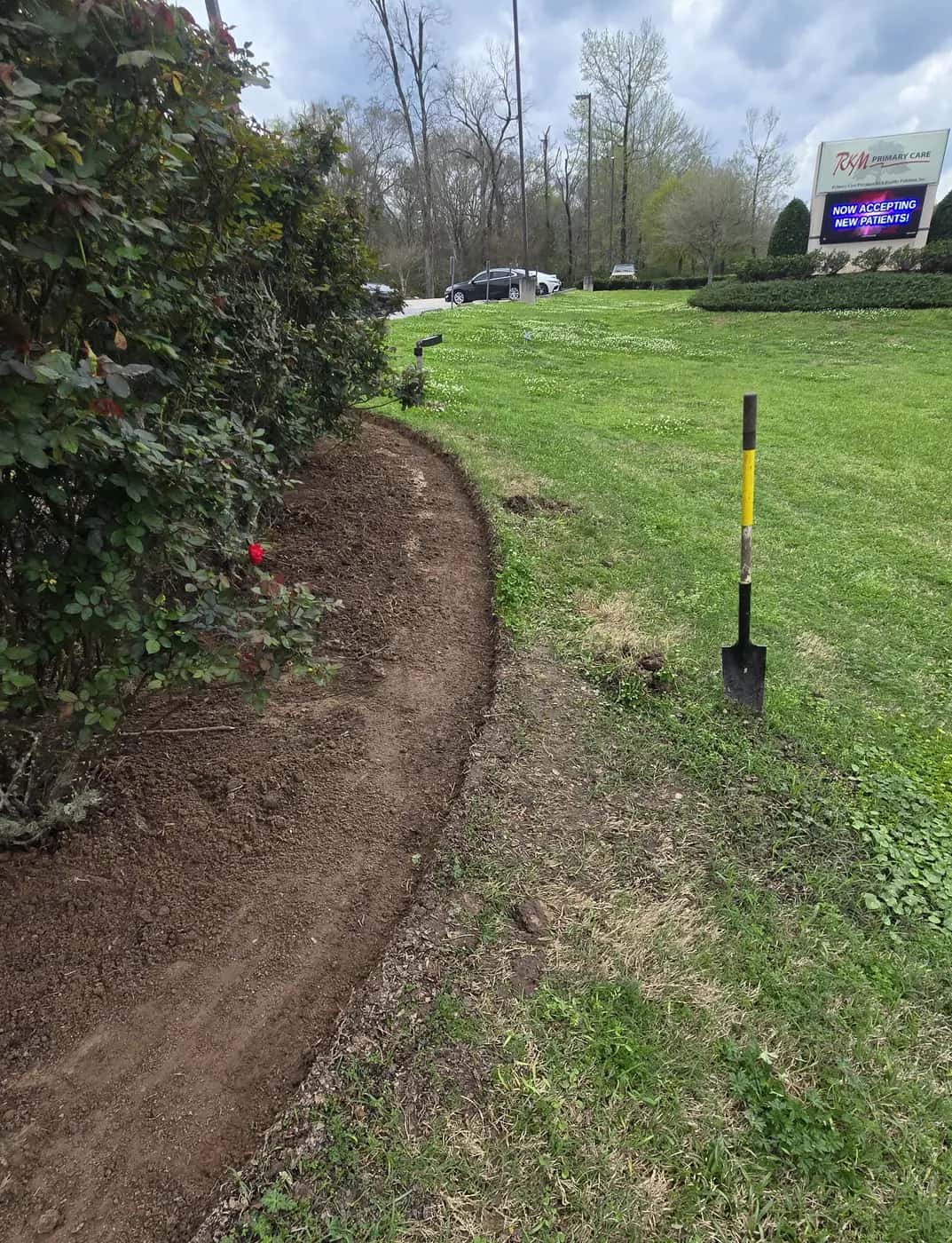 Freshly cut curved bed edge along a commercial front bed in Clinton, LA, with an edging spade standing in the grass.