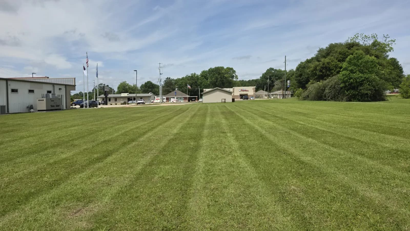 Large open lawn with long professional mowing stripes beside commercial buildings.