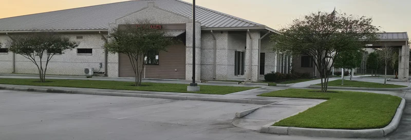 Commercial lawn mowing result in Livingston, LA: trimmed turf islands and crape myrtles around a medical office parking lot.