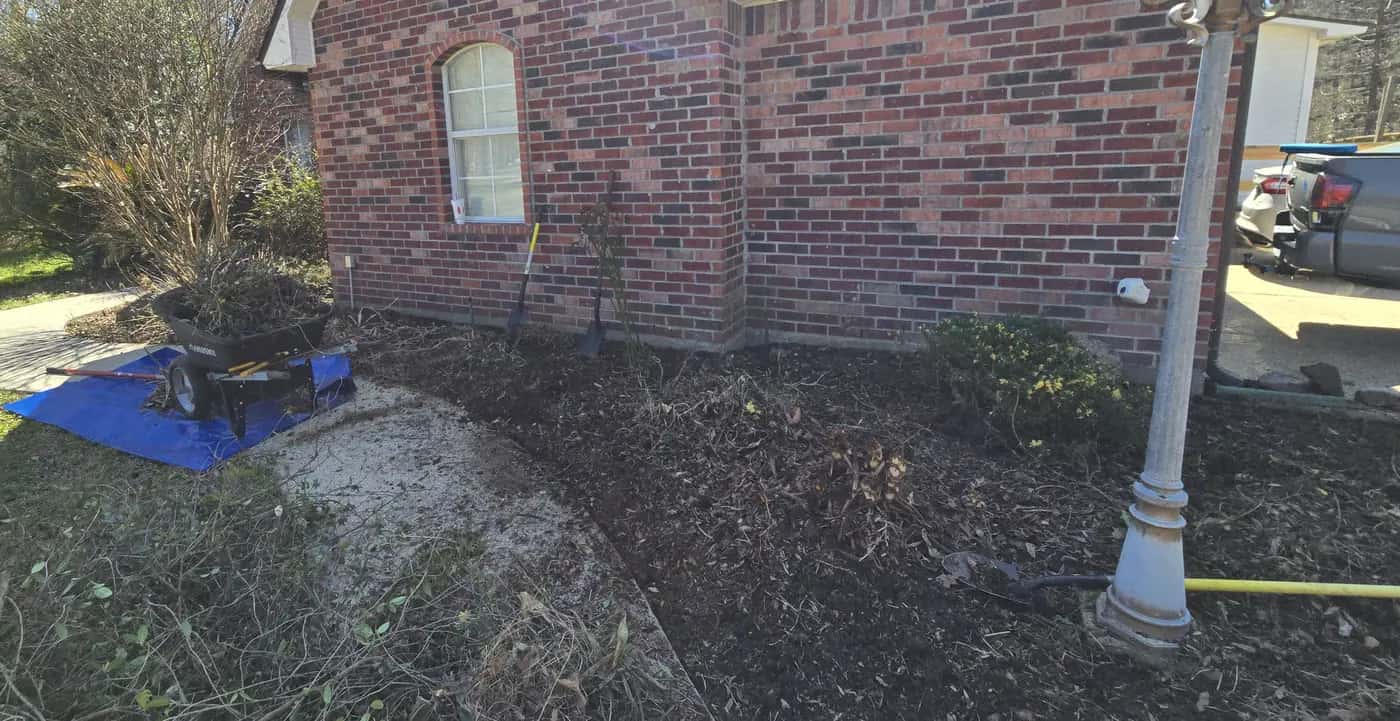 Before: bare, patchy flower bed along a brick house wall in Walker, LA, ready for a new landscape install.