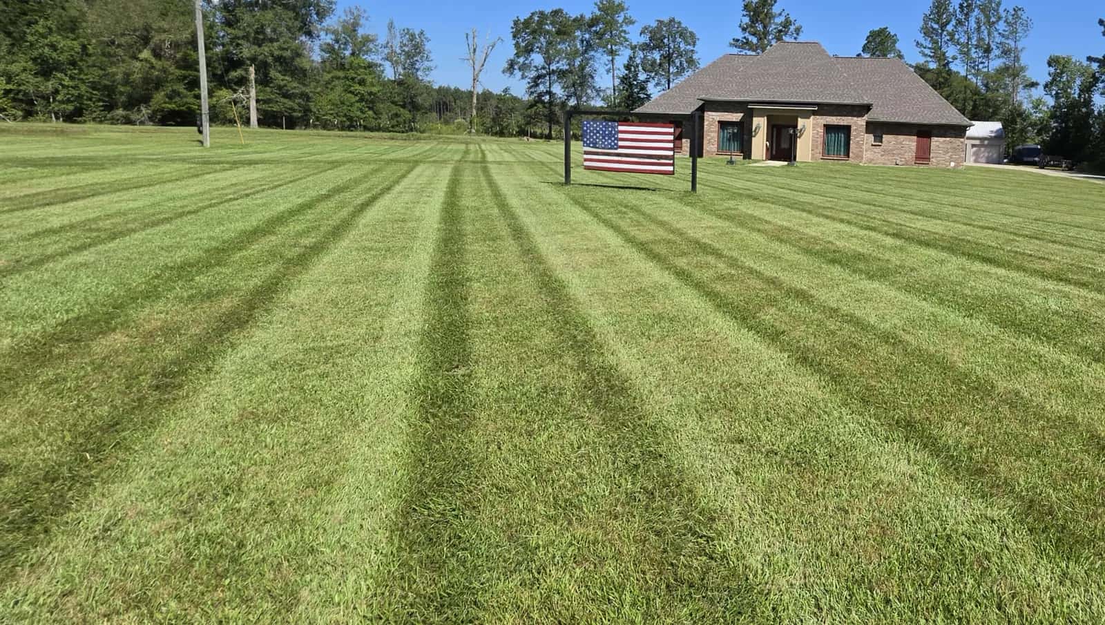 Freshly mowed front lawn with crisp diagonal stripes on Weiss Rd in Walker, LA, with an American flag and brick house in the background.